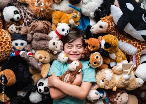 Happy young boy surrounded by his stuffed animals shot from above.
