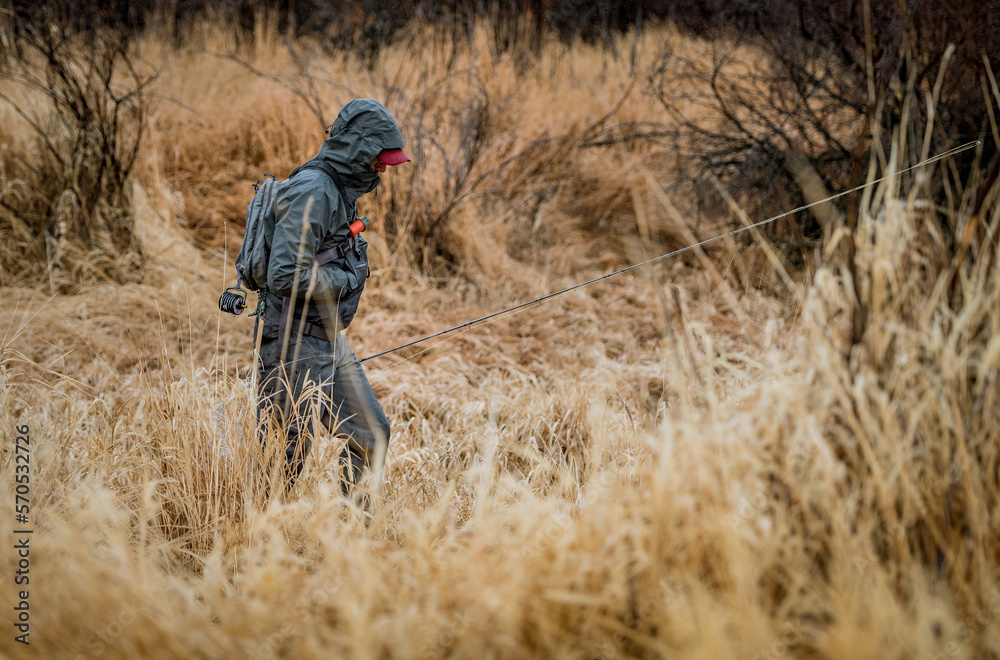 Fly fisherman in waterproof clothing walking through field Fly fisherman in waterproof clothing walking through field