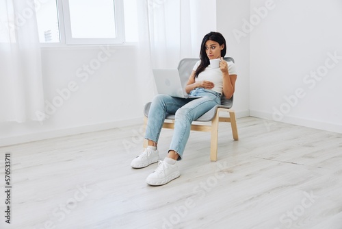 Woman relaxing at home sitting in a chair and watching a movie on her laptop with a cup of tea, the surprise of watching, freelancer lifestyle