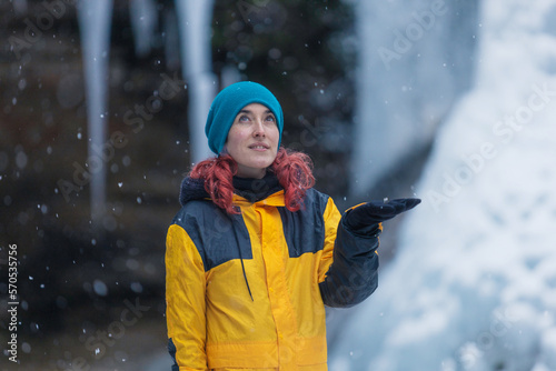 redhead young woman with red in a waterfall of nine in the mountain while snowing, copy space