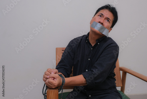 Man sitting on armchair with hands tied up and mouth sealed