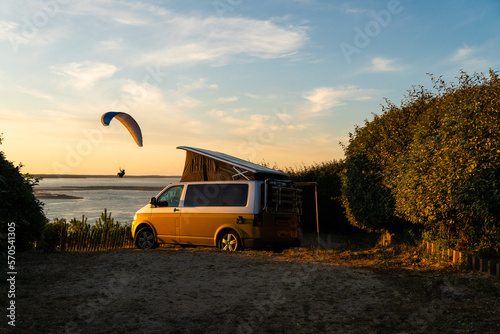 paraglider in golden sunset near her mini van and looking on the ocean at summer in camping natural area