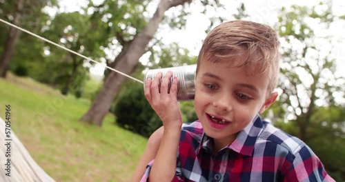 Cute little Boy curiously listening on tin can phone in park, concept for telephone or mobile communication. photo