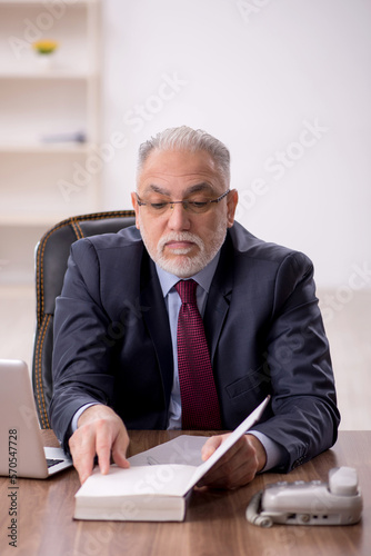 Old male boss reading book at workplace