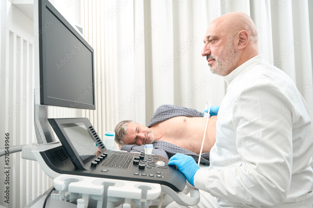 Handsome ultrasound specialist is examining health of patient in the clinic Handsome ultrasound specialist is examining health of patient in the clinic