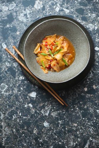 Korean traditional kimchi in a dark-olive bowl, above view on a dark-brown granite background, vertical shot, copy space