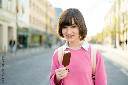 Pretty teenage girl eating tasty fresh ice cream outdoors on warm and sunny summer day. Children eating sweets.