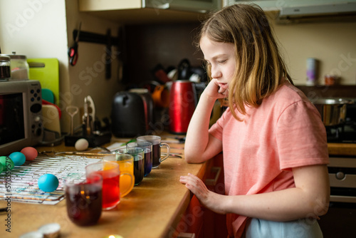 Pretty preteen girl dyeing Easter eggs at home. Child painting colorful eggs for Easter hunt. Kid getting ready for Easter celebration.
