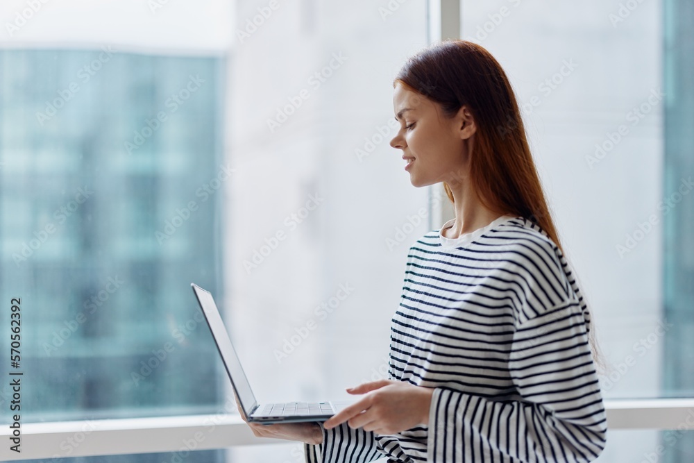 Business woman freelancer working in the city near a window and holding a laptop, working with technology online