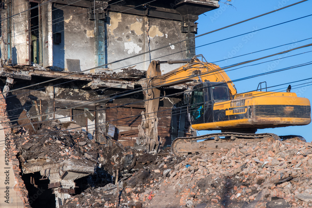 Yellow crawler excavator taking apart a building. Wires as guidlines on foreground Yellow crawler excavator taking apart a building. Wires as guidlines on foreground