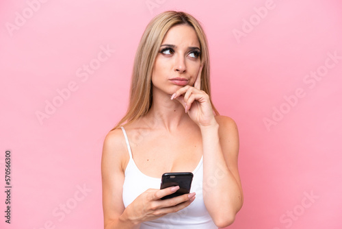 Pretty blonde woman isolated on pink background using mobile phone and thinking