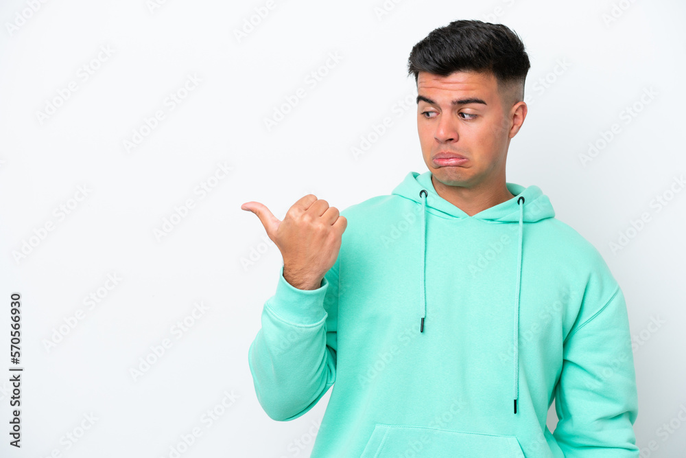 Young caucasian handsome man isolated on white background unhappy and pointing to the side Young caucasian handsome man isolated on white background unhappy and pointing to the side