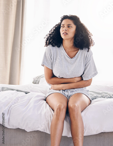 Black woman, sick and stomach ache on house bed, home or bedroom in period pain, menstruation cramps or ibs crisis. Hurt person, injury and abdomen tummy in healthcare emergency or appendicitis risk photo