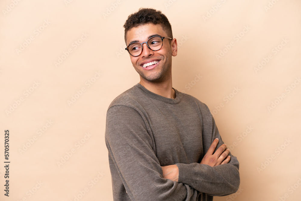 Young Brazilian man isolated on beige background with arms crossed and happy Young Brazilian man isolated on beige background with arms crossed and happy