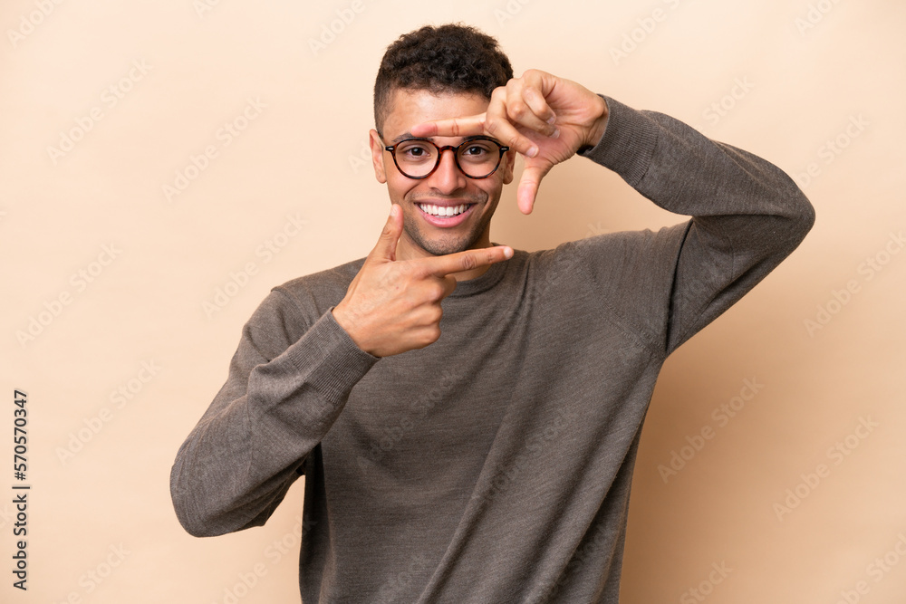 Young Brazilian man isolated on beige background focusing face. Framing symbol Young Brazilian man isolated on beige background focusing face. Framing symbol