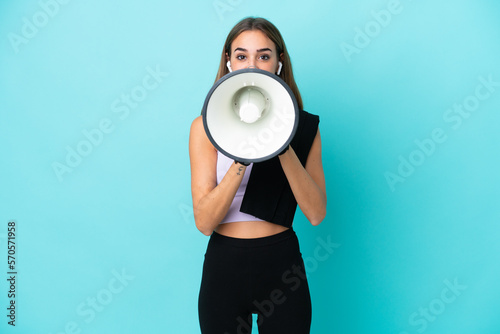 Young sport woman isolated on blue background shouting through a megaphone