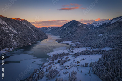 The beautiful setting of the Weissensee Nature Park. Frozen Lake Weissensee, Carinthia, Alps, Austria. Aerial drone shot in January 2022. Sunset time.