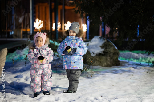 Two little girls with cup of hot chocolate at night city in the winter.  Sisters drink hot drinks.