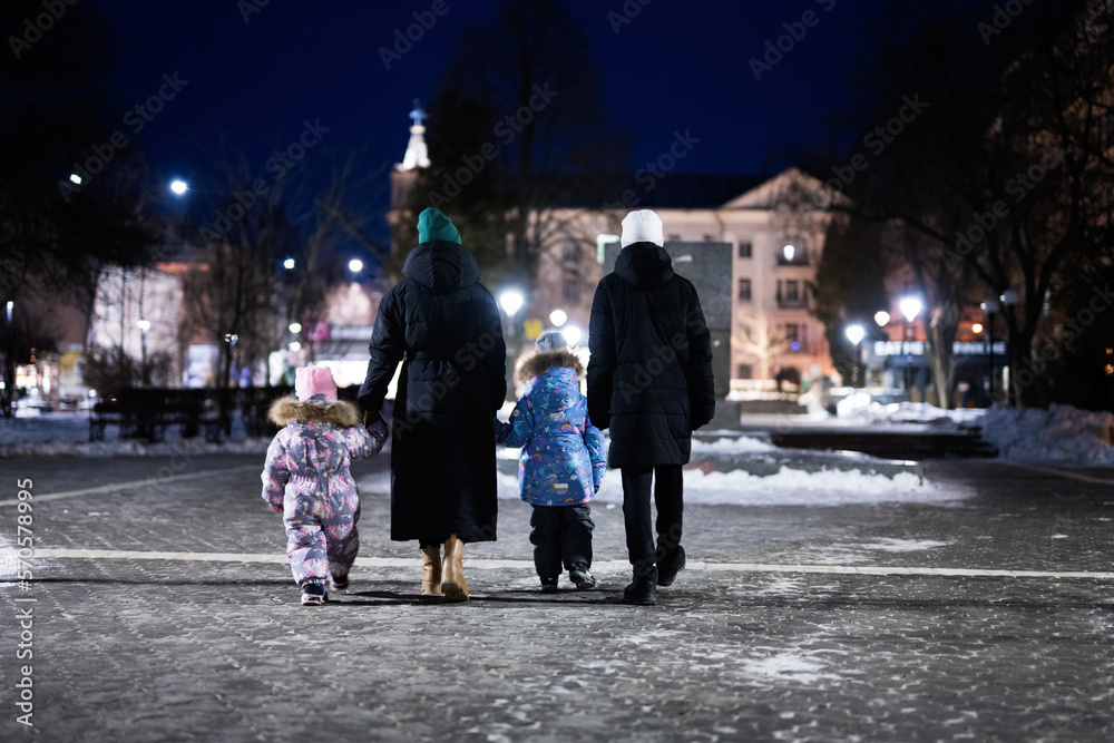 Back of family walk through the night city in the winter. Mother and three children in evening.
