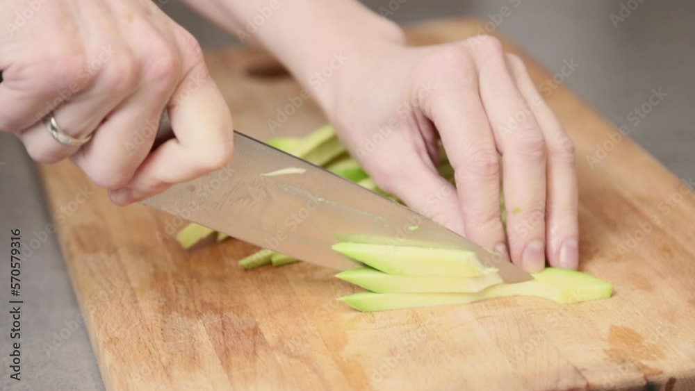 Woman cutting an avocado into pieces on the cutting board in the kitchen. Vegan breakfast snack. Video in slow motion. Woman cutting an avocado into pieces on the cutting board in the kitchen. Vegan breakfast snack. Video in slow motion.
