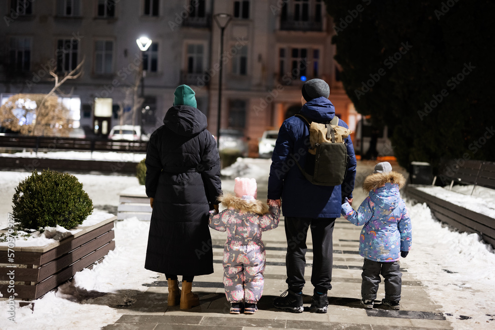 Back of family with two kids walk through the night city in the winter.