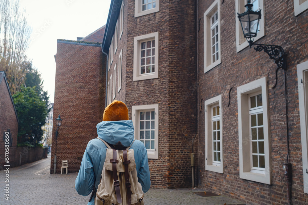 winter travel to Dusseldorf, Germany. young Asian tourist in blue jacket and yellow hat (symbol of Ukraine) walks through sights of old town or Altstadt. Popular center of Rheinland and Westphalia winter travel to Dusseldorf, Germany. young Asian tourist in blue jacket and yellow hat (symbol of Ukraine) walks through sights of old town or Altstadt. Popular center of Rheinland and Westphalia