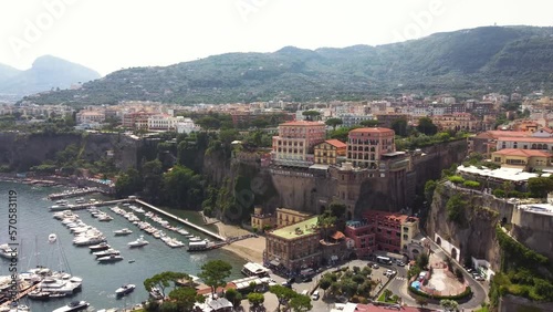 Aerial drone sea view footage of Sorrento summer resort, port, skyline and steep cliff coastline in Campania, Italy. The marina piccola with ships and yachts docked, hotels and town.