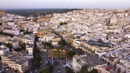 Aerial drone footage of Ostuni - La Citta Bianca (white city), Puglia, Italy at sunset. View of main street to the medieval historic old town, landmark tourist destination and new part from above.