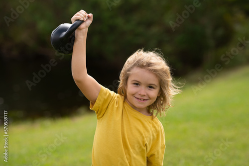 Kid lifting the kettlebell in park outside. Sport child workout. Child exercising with kettlebell. Sporty child with dumbbell. Fit kids training.