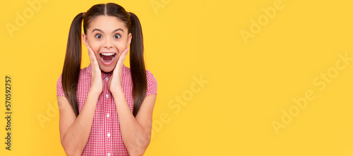 Shocked eye-popping tween girl show surprise yellow background, OMG. Child face, horizontal poster, teenager girl isolated portrait, banner with copy space. © Olena
