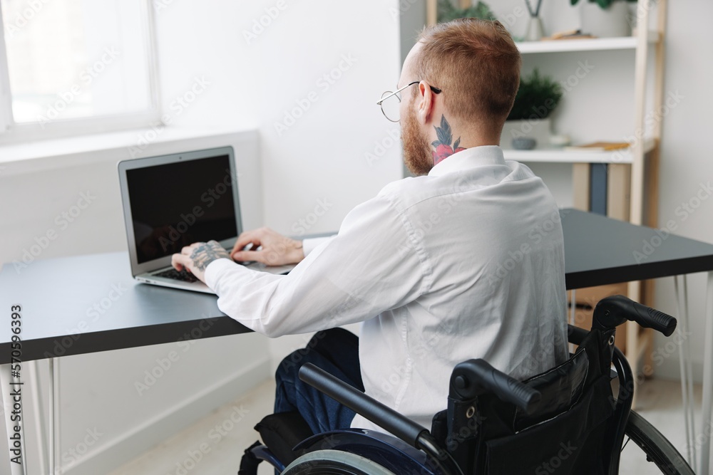 man wheelchair businessman with tattoos in the office works at a laptop online, business process from the back, copy space, integration into society, the concept of working a person with disabilities man wheelchair businessman with tattoos in the office works at a laptop online, business process from the back, copy space, integration into society, the concept of working a person with disabilities