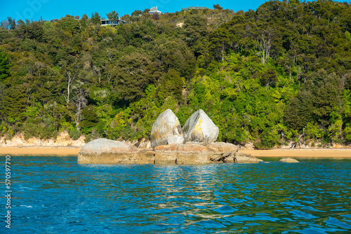 Geteilter Felsbrocken im blauen Meer mit grüner und felsiger Küste in Neuseeland im Abel Tasman Nationalpark am Split Apple Rock. photo