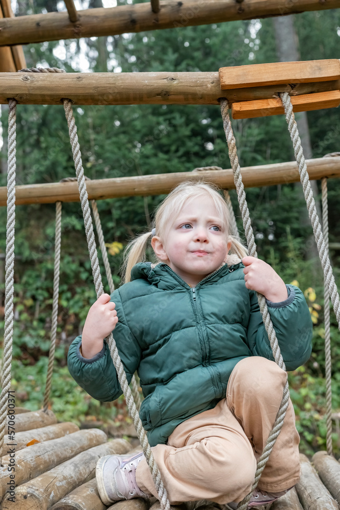 Portrait of anxious little girl in fall on suspension bridge or playground. Girl wears warm bologna jacket. Portrait of anxious little girl in fall on suspension bridge or playground. Girl wears warm bologna jacket.