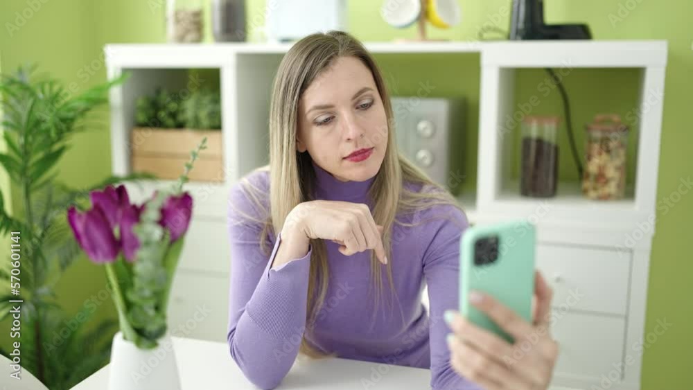 Young blonde woman having video call sitting on sofa at home