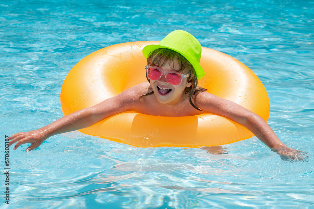 Child swin in swimming pool on inflatable ring. Kid swim with orange float. Water toy, healthy outdoor sport activity for children. Fashion summer kids in hat sunglasses.