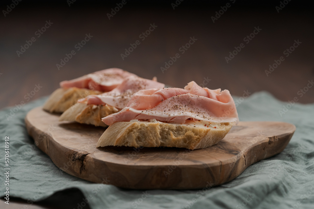 Toassted baguette slices with prosciutto cotto and cream cheese on olive wood board