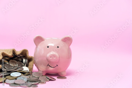 Pink piggy bank with many money coin on pink background