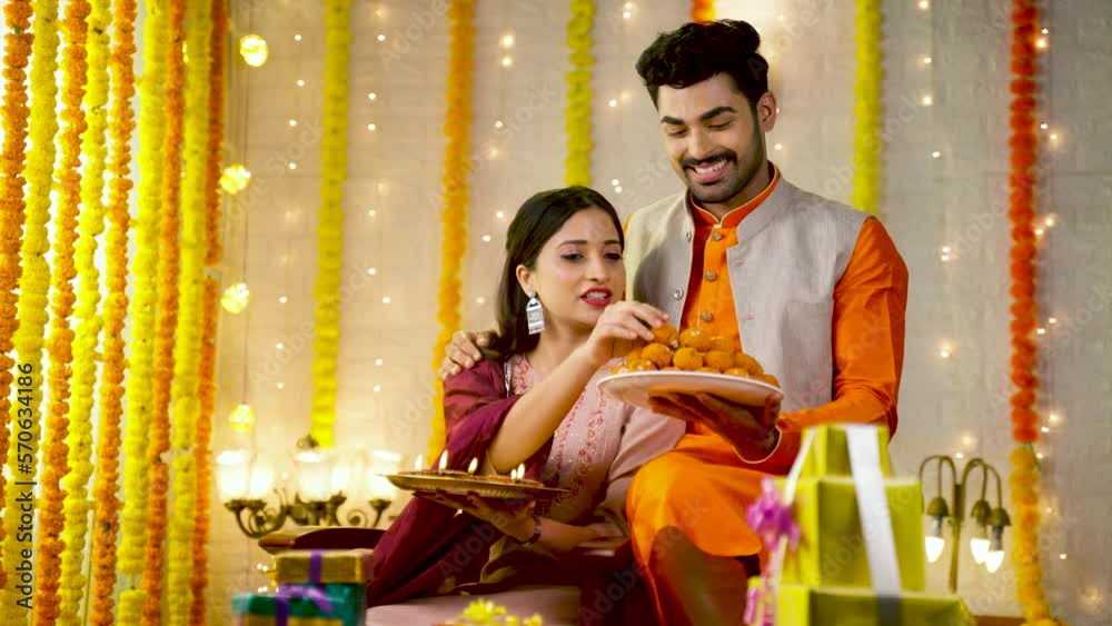 happy smiling young couple in traditional ethnic wear looking at camera while preparing for festival at home - concept of diwali festive celebration, greeting and family relationship