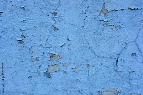 The gray flat concrete wall painted long ago with blue, light blue paint has already cracked, deep cracks on the wall are visible and it has peeled off in a long time. photo