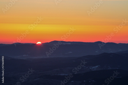 Orange sky at sunrise in dark winter mountains