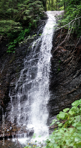 A high waterfall falls in the middle of a green forest