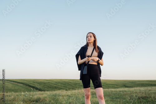 A beautiful woman in casual clothes is standing in a summer sunset in an endless field and looking away with a serious face.