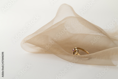 Złoty pierścionek zaręczynowy na walentynki leżący na tiulu na jasnym tle