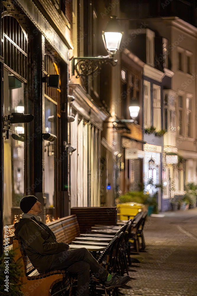 The Hague, Netherlands A man sits at outdoor restaurant tables at night.