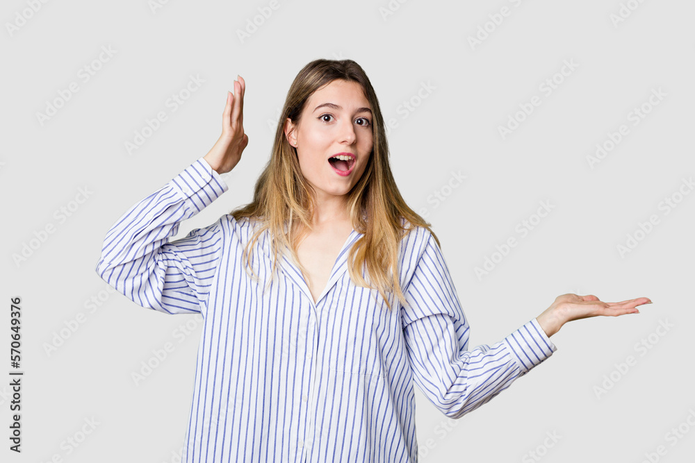 Young blonde posing for a portrait isolated, exuding natural beauty and radiance holds copy space on a palm, keep hand over cheek. Amazed and delighted. Young blonde posing for a portrait isolated, exuding natural beauty and radiance holds copy space on a palm, keep hand over cheek. Amazed and delighted.