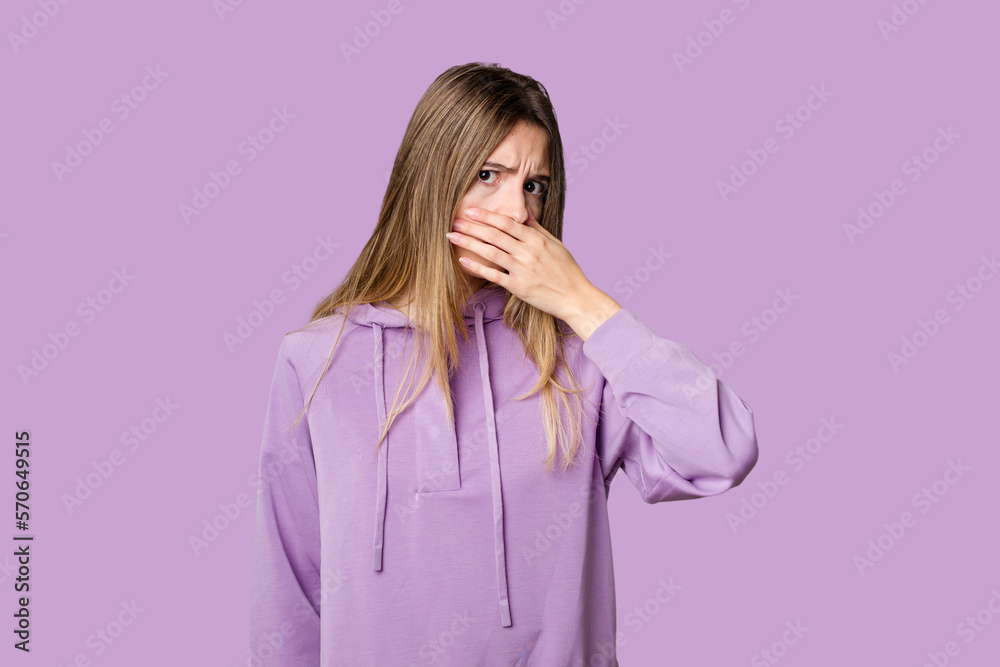 Young blonde posing for a portrait isolated, exuding natural beauty and radiance covering mouth with hands looking worried. Young blonde posing for a portrait isolated, exuding natural beauty and radiance covering mouth with hands looking worried.