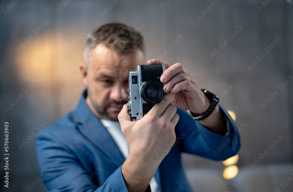 A bearded man in a suit holds a vintage film camera. Shot on a gray background. A bearded man in a suit holds a vintage film camera. Shot on a gray background.