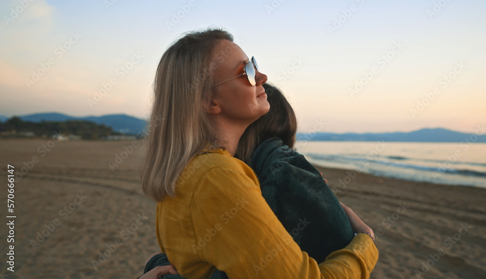 Mother cover his daughter with blanket and hugging on the beach at sunset. Mother cover his daughter with blanket and hugging on the beach at sunset.
