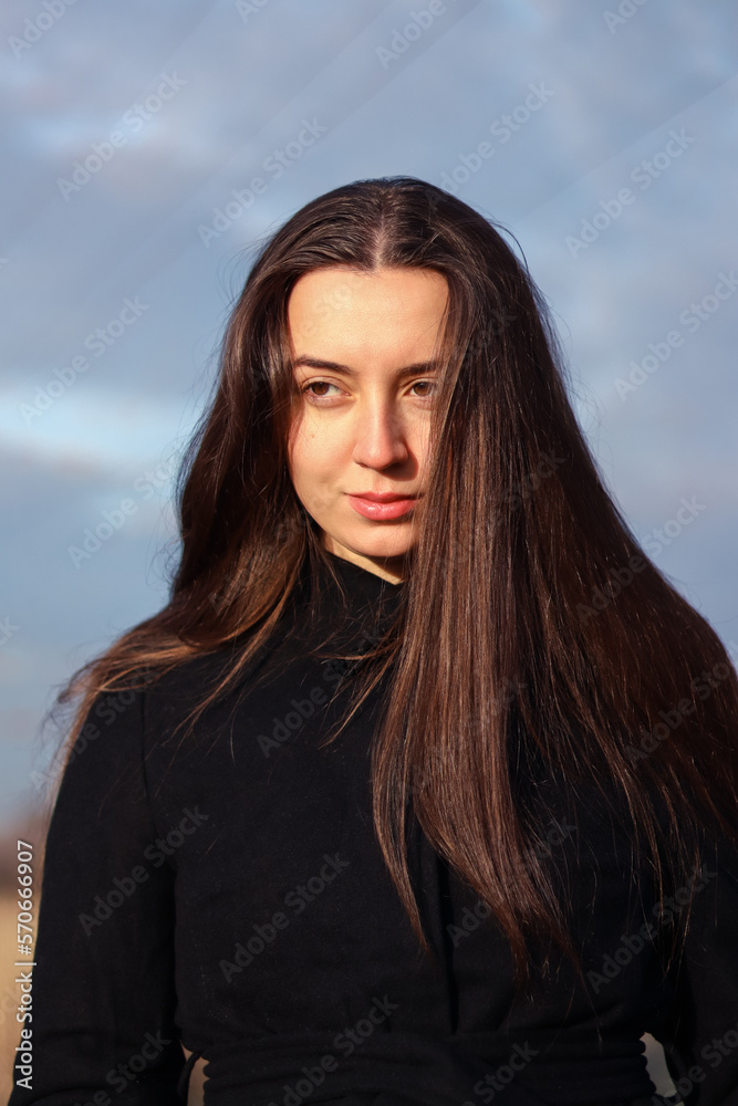 Portrait of a woman. Portrait of a brunette girl. Beautiful face. Woman in black clothes. Long brown hair. Portrait photo in nature. The woman is wearing a black coat. Natural beauty. Without makeup.