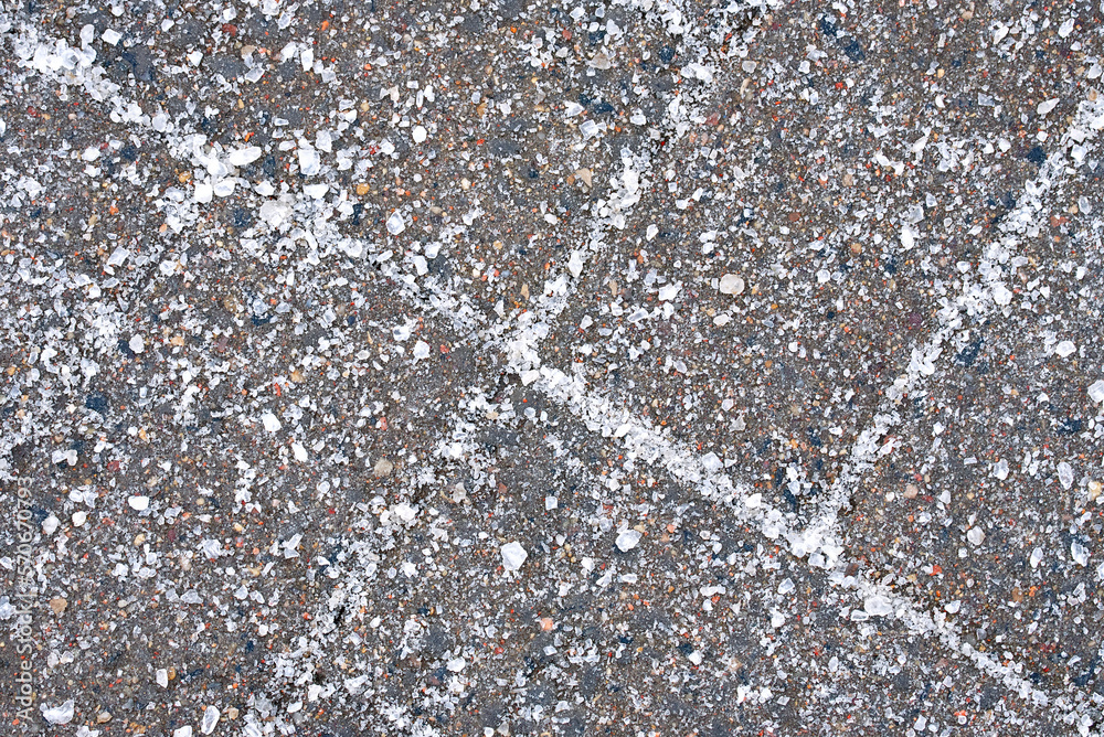 Salt grains on paving slabs closeup. Salted sidewalk, slipping